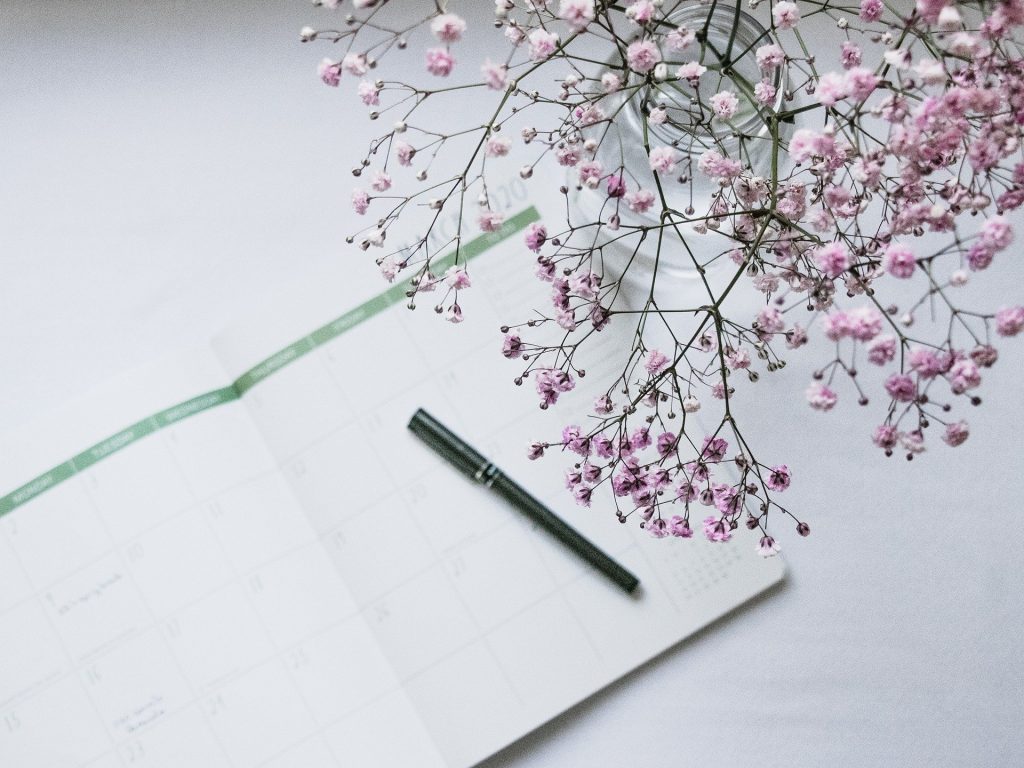 A planner with a pen next to a vase of pink flowers