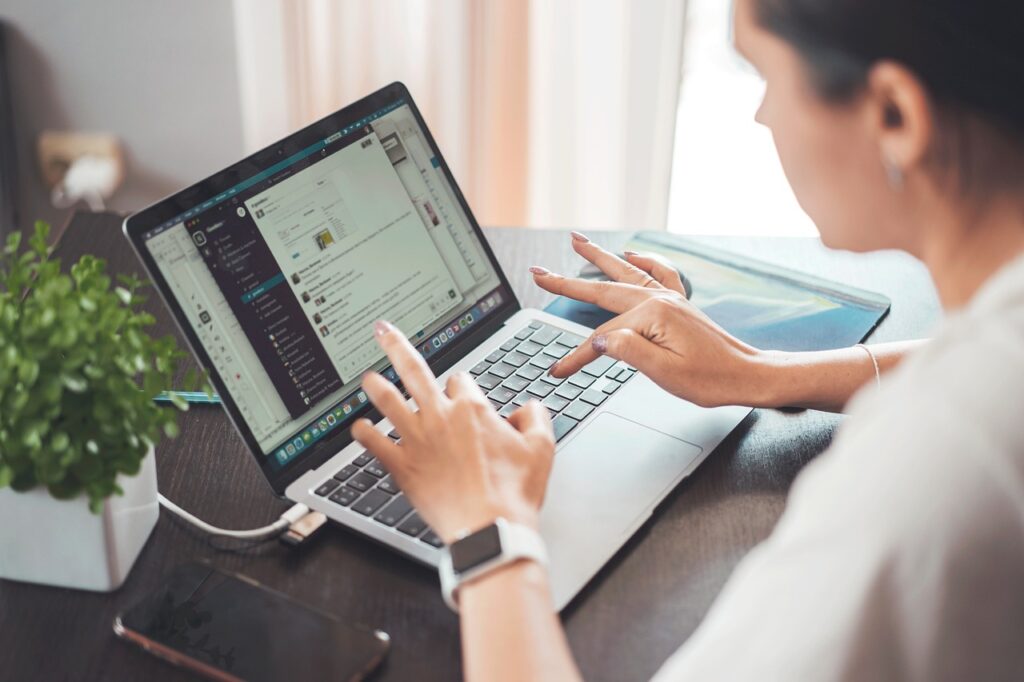 Woman types on a laptop sitting on top of a brown coffee table.